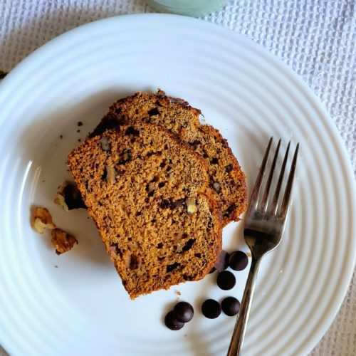 Photo of banana bread slices on a plate garnished with chocolate chips and walnuts.