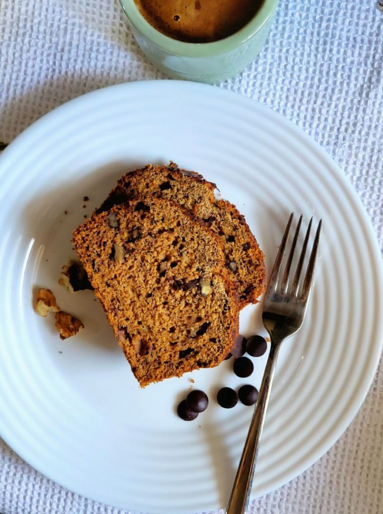 Photo of banana bread slices on a plate garnished with chocolate chips and walnuts.